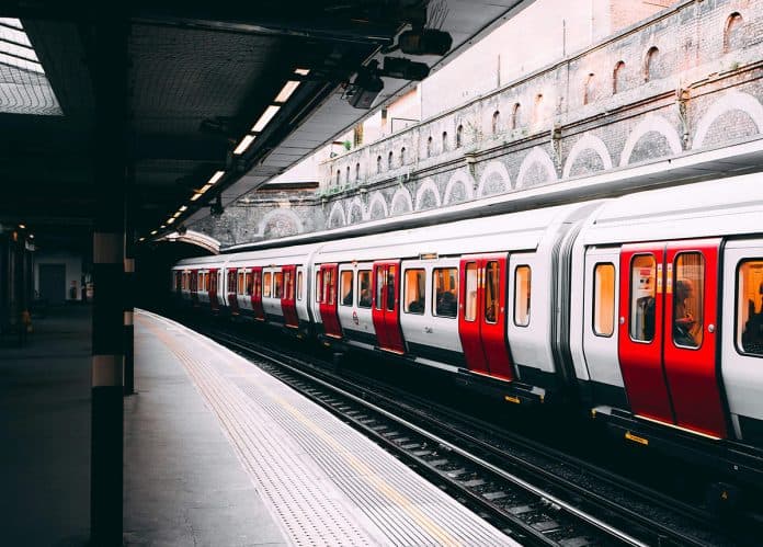 A red and white train is stationed on a platform with an arched ceiling and empty tracks.