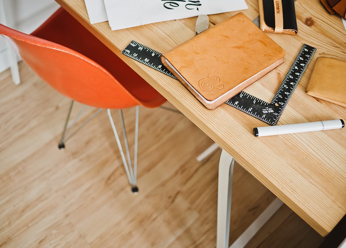 Photo of an orange chair and a desk with office supplies like rulers and a notebook.