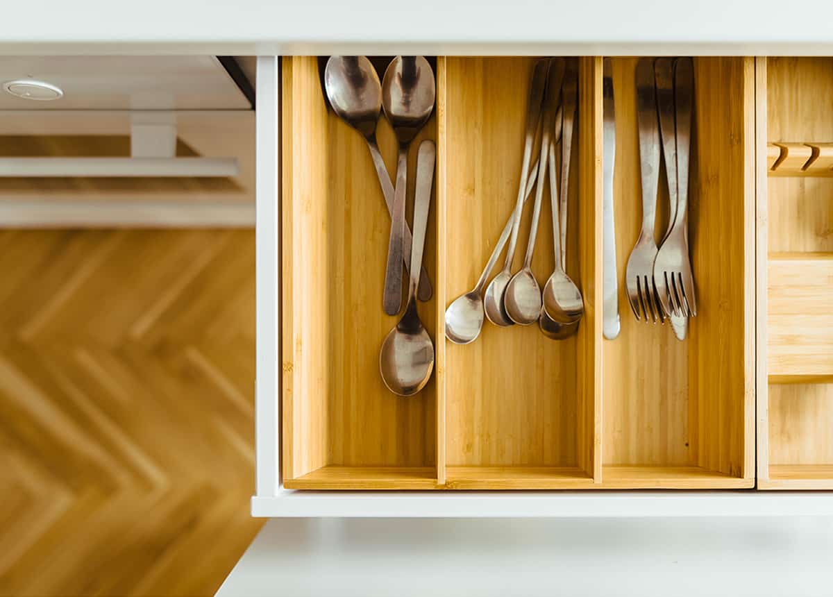 Top-down view of a neatly organized cutlery drawer with sections for spoons and forks in a wooden divider.