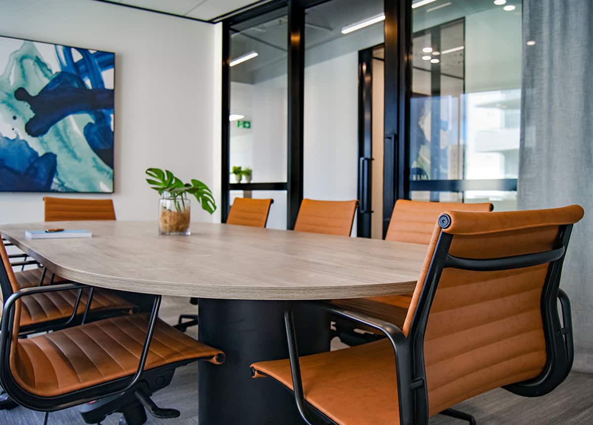 Modern conference room with leather chairs around a wooden table, featuring a large abstract painting on the wall.