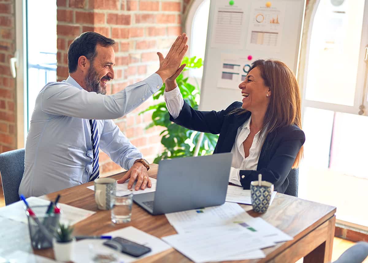 Two business professionals giving a high five across a table in a bright office setting.